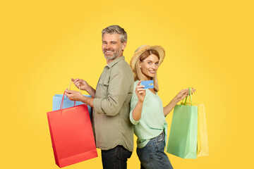 Season sales concept. Cheerful european middle aged spouses carrying colorful shopping bags and showing credit card