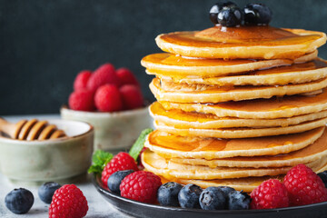 Delicious pancakes, with fresh blueberries, raspberry and maple syrup or honey on a dark background