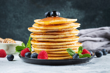 Delicious pancakes, with fresh blueberries, raspberry and maple syrup or honey on a dark background