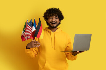 Smiling indian man holding laptop and flags of different countries - obrazy, fototapety, plakaty
