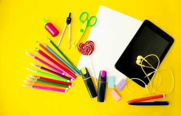 On a yellow background, school supplies, a laptop, pencils, felt-tip pens, scissors, a magnifying glass.  Concept back to school, online learning.  Flat lay, top view, copy space for text. 