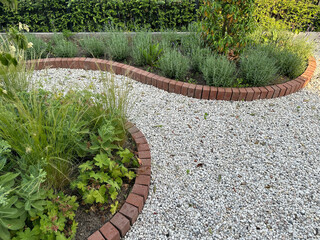 Stone pathway in the garden. Fragment of front garden with grey gravel. Flower beds and brick borders - obrazy, fototapety, plakaty