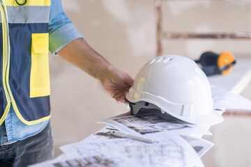 Architect reaching hand to take hardhat on heap of project papers at construction site man in vest ready for reconstruction process in house safety rules and equipment