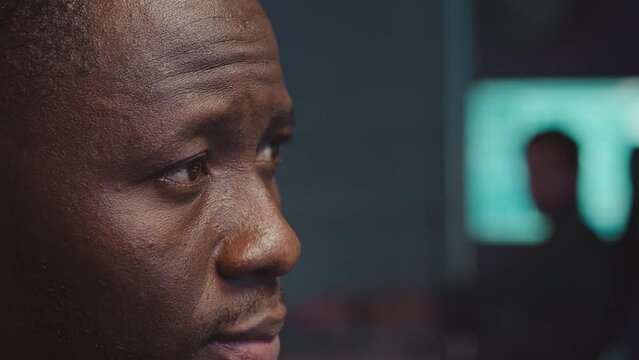 Side view closeup of young Black man looking at computer desktop while analyzing data info working ay cybersecurity agency at night