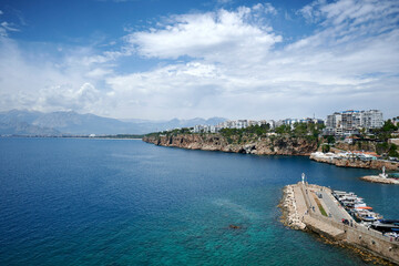 Breathtaking coastal view in Antalya, with blue ocean, lighthouse, and sailing vessel.