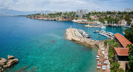 Breathtaking coastal view in Antalya, with blue ocean, lighthouse, and sailing vessel.