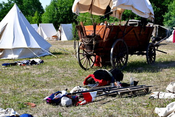 A close up on an old, historical, Napoleonic period tent with some armor, suits, and rifles arranged to create a circle situated next to some bags full of sand seen on a sunny summer day in Poland - Powered by Adobe