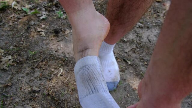 Close up of dirty white socks being removed from from feet while standing shoeless on sandy ground.