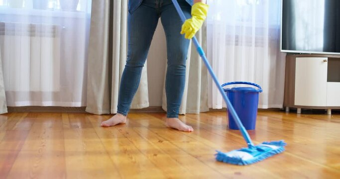 Woman in casual clothes washing a wooden floor with a damp microfiber mop