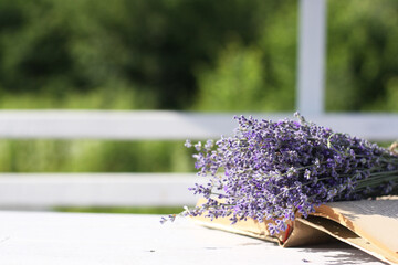 Lavender bouquet laid over an old book on a white wooden table. Vintage style. Photo with empty...