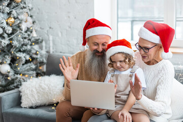 Attractive active grandfather and grandmother, senior man and woman, with grandchild doing video call with parents on laptop or smartphone. Concept of spending vacations or holidays at grandparents. 