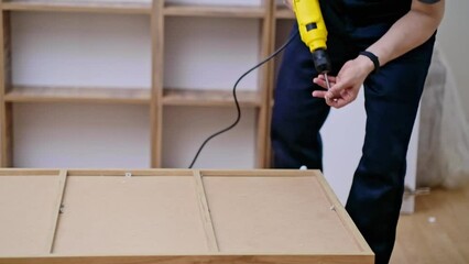Custom furniture assembling handyman fixing fasteners on wooden cabinet back side with professional screwdriver quality carpentry services specialist working with wood materials