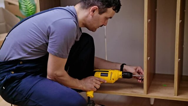 Furniture assembly process focused firm worker in overalls using screwdriver to install shelf holders into wooden rack stylish furniture design for living room interior