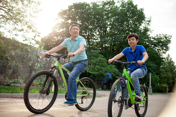asian old father and son ride bikes together in the park, korean senior and grandpa are active with...