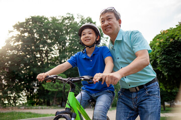asian dad teaches son to ride bike, korean senior helps child, boy in helmet is actively relaxing...