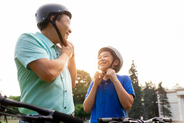 asian father and son put helmet on head before riding bikes, korean senior with son outdoor activities together