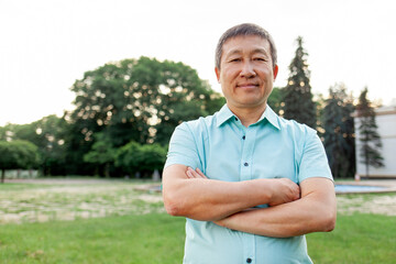 portrait of asian elderly man wearing shirt in park, korean pensioner standing with arms crossed...