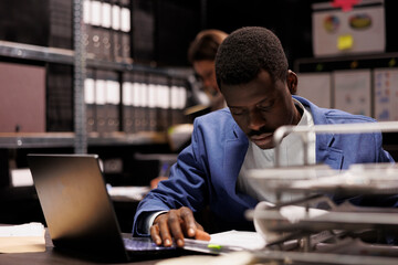 Businessman analyzing administrative files, searching for bureaucracy record in corporate depository. African american bookkeeper working late at night at accountancy report