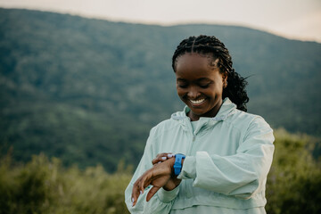 Black fitness woman jogging and using a smartwatch in the nature during the sunset.