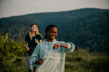Active Lifestyle in the Wilderness: Embracing an active lifestyle, black and white female joggers navigates a trail in a lush forest, using their smartwatch to maintain their pace and monitor their ov