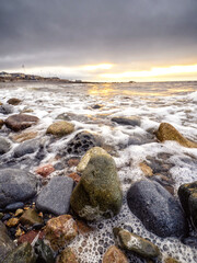 Rough stone beach by Blackrock diving tower in Salthill, Galway city, Ireland. Dark cloudy sky before sunrise. Calm nature scene. Selective focus.