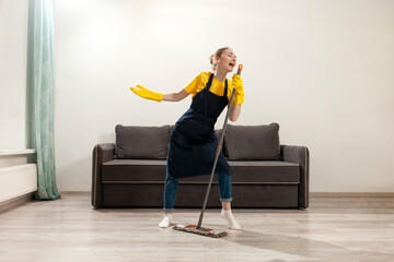 young happy housewife girl in apron and gloves washes the floor with mop and dances