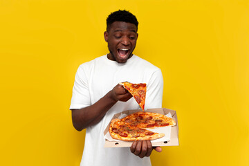 joyful african american man in white t-shirt holds box of pizza on yellow isolated background, guy with fast food