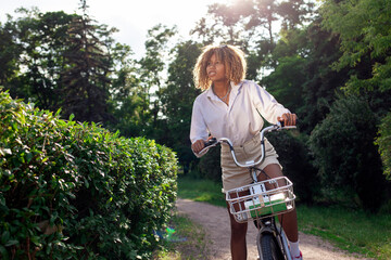 Fototapeta na wymiar african american curly girl rides bike in the park in summer and looks away at copy space