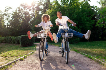 african american crazy couple quickly ride forward in the park on bicycles and scream, man and woman fly