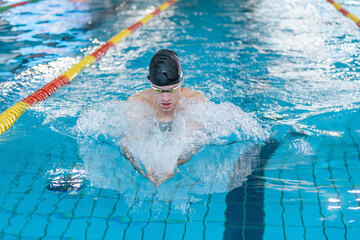 Front view of a male athlete swimming breaststroke style in the pool between two swimming lane markers. Competitive swim discipline concept. - Powered by Adobe