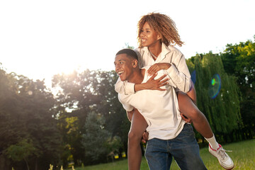 african american happy couple walk together in park in summer and look at copy space, man carries woman