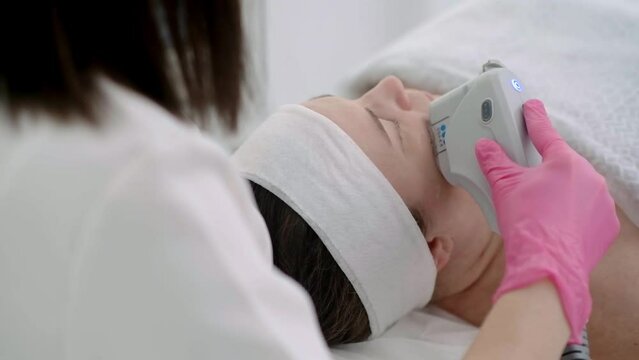 Using professional equipment at a beauty center, a SMAS ultrasound face lifting massage is given to a relaxed female client. 