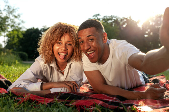 african american young couple lies in the park in the summer on the grass and takes selfie