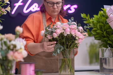 Flower decorator professional. Closeup of hands of young woman florist creating bouquet of pink roses on the table