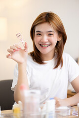 Lovely Asian girl using eyelash curler on long eyelash before applying mascara brush in morning make up routine.
