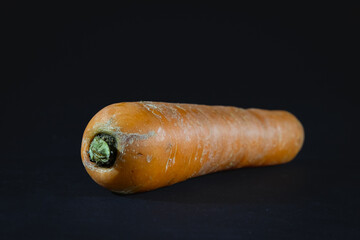 Selective blur on an Orange carrot isolated on a black background in a studio shot, unpeeled, a single carrot, ready to be prepared.