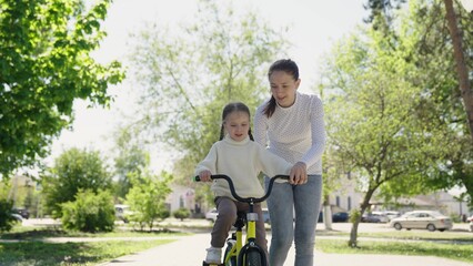 mother teaches her daughter ride bike park. happy family childhood dream., dream kid, mother helps her daughter, parent horseback riding with daughter, sunny spring day, parent guardian mom teaching