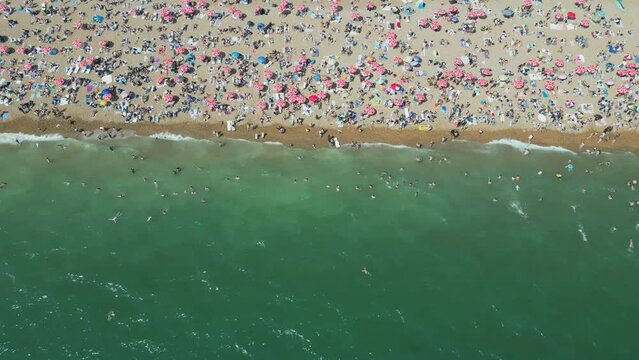Drone footage of a crowded beach with turquoise water in summer.