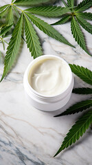 Fototapeta na wymiar White jar of face cream stands on a marble background, surrounded by marijuana leaves