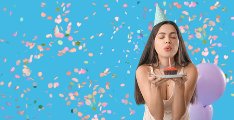 Happy young woman blowing out candle on muffin against light blue background. Banner for design - Powered by Adobe