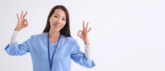 Female Asian doctor showing OK gesture on white background with space for text