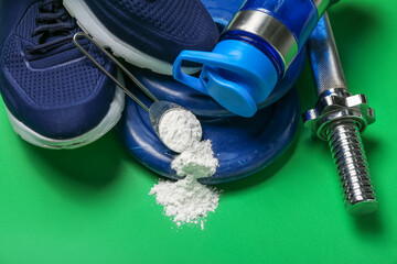 Scoop with amino acid supplement, sports equipment, shoes and bottle of water on green background,...