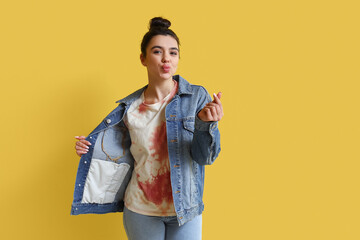 Young woman in tie-dye t-shirt making heart with her fingers on yellow background