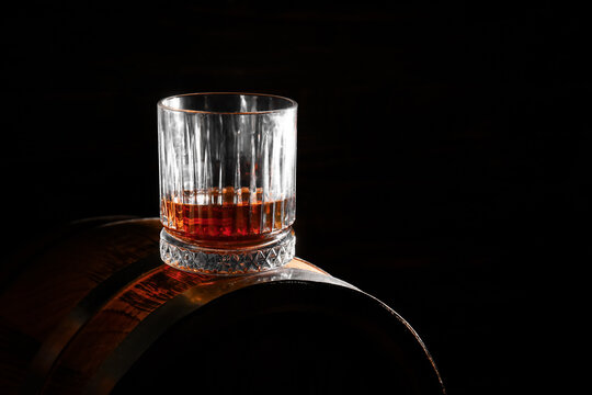 Barrel with glass of rum on black background