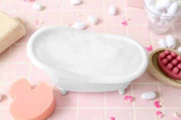 Fototapeta na wymiar Small bathtub with foam and bath supplies on color tile background