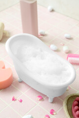 Fototapeta na wymiar Small bathtub with foam and bath supplies on color tile table