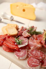 Board with assortment of tasty deli meats on white wooden background, closeup