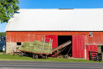 Square hay bales on hay wagon with elevator going into hay loft in barn.