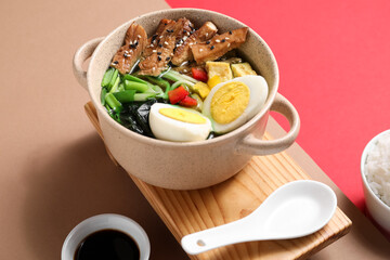 Cooking pot with tasty Chinese soup and soy sauce on color background
