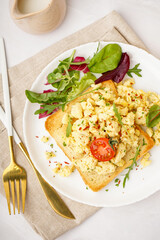 Plate with tasty scrambled eggs sandwich and salad on light background